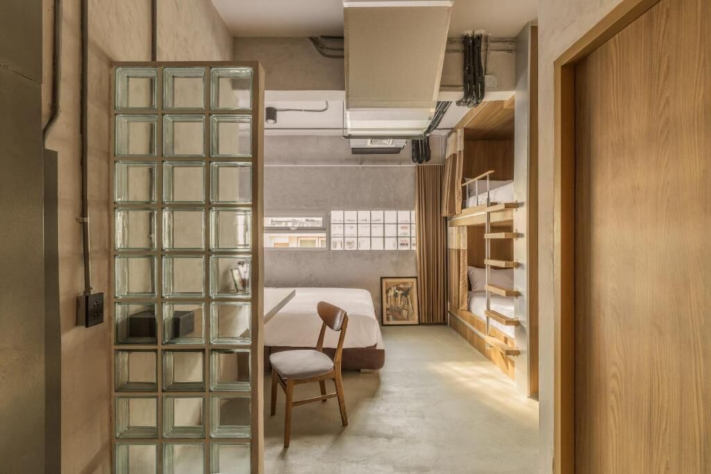 Une chambre à coucher de taille réduite, comprenant un lit, une chaise, une cloison en verre et une armoire en bois.