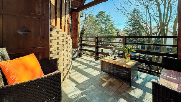A wooden balcony with wicker furniture, a brick wall, and a view of trees and buildings. - Holiday home near the water with air conditioning and Wi-Fi (Zamárdi)
