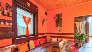 A cozy room with a wooden bench, a table with a floral tablecloth, and a window with a red curtain. - Holiday home near the water with air conditioning and Wi-Fi (Zamárdi)