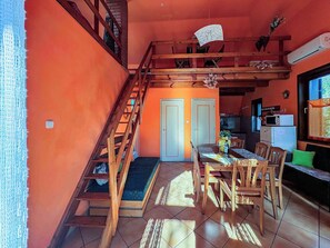 Un coin repas avec un escalier en bois, une table dressée pour quatre personnes et une cuisine en arrière-plan.
