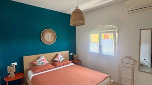 Een slaapkamer met een bed, een hanglamp, een spiegel, een raam en een klein tafeltje.