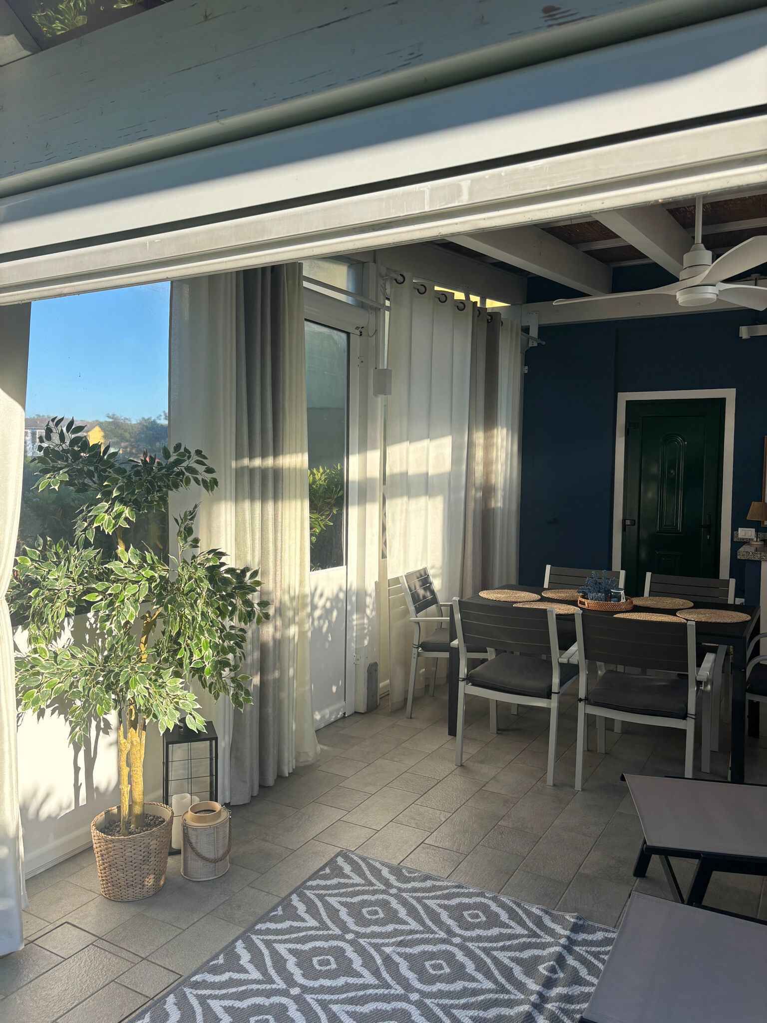 An outdoor patio with a table and chairs, a ceiling fan, and a view of the sky.