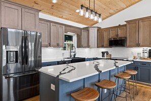 A modern kitchen with stainless steel appliances, wooden cabinets, and a large island with bar stools. - Private Luxe Cabin: Views+EV Charger+Hot Tub+Fire Pit+Bowling+Kids Play Area (Mineral Bluff)