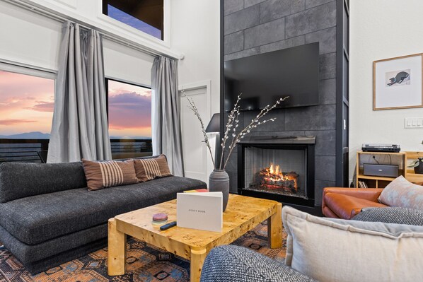 Una sala de estar moderna con chimenea, un sofá, una mesa de centro y vistas al atardecer.