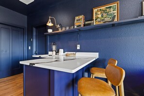 Una cocina con pared azul de acento, una isla blanca, sillas de madera, una cafetera y un radio antiguo.
