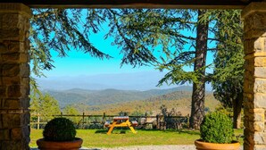 Un arc de pedra emmarca una vista d'una taula de pícnic i dues plantes en testos en una zona verda amb un fons de muntanyes.