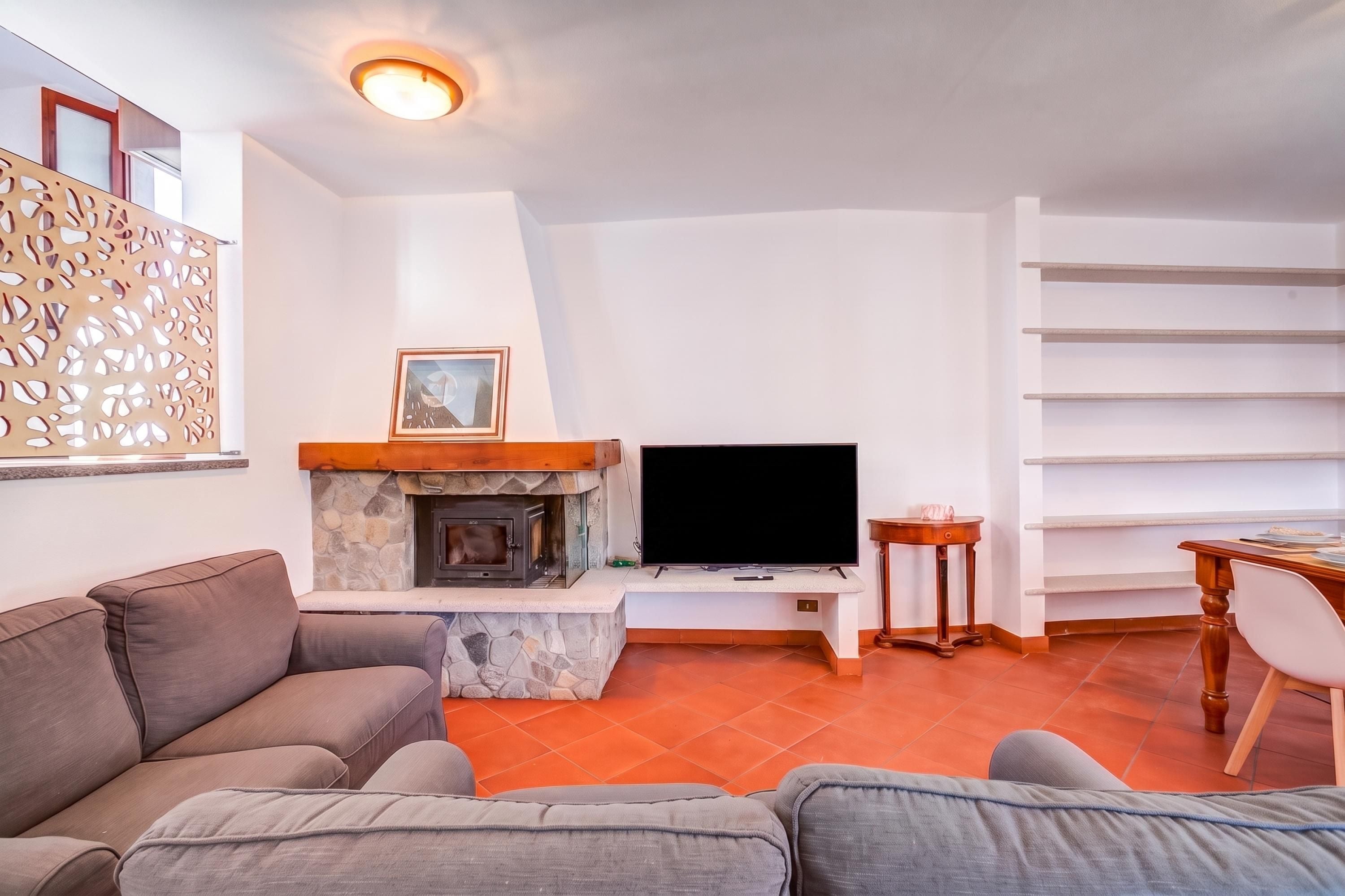 A living room with a stone fireplace, a flat-screen TV, a sofa, and a dining area with a table and chairs.