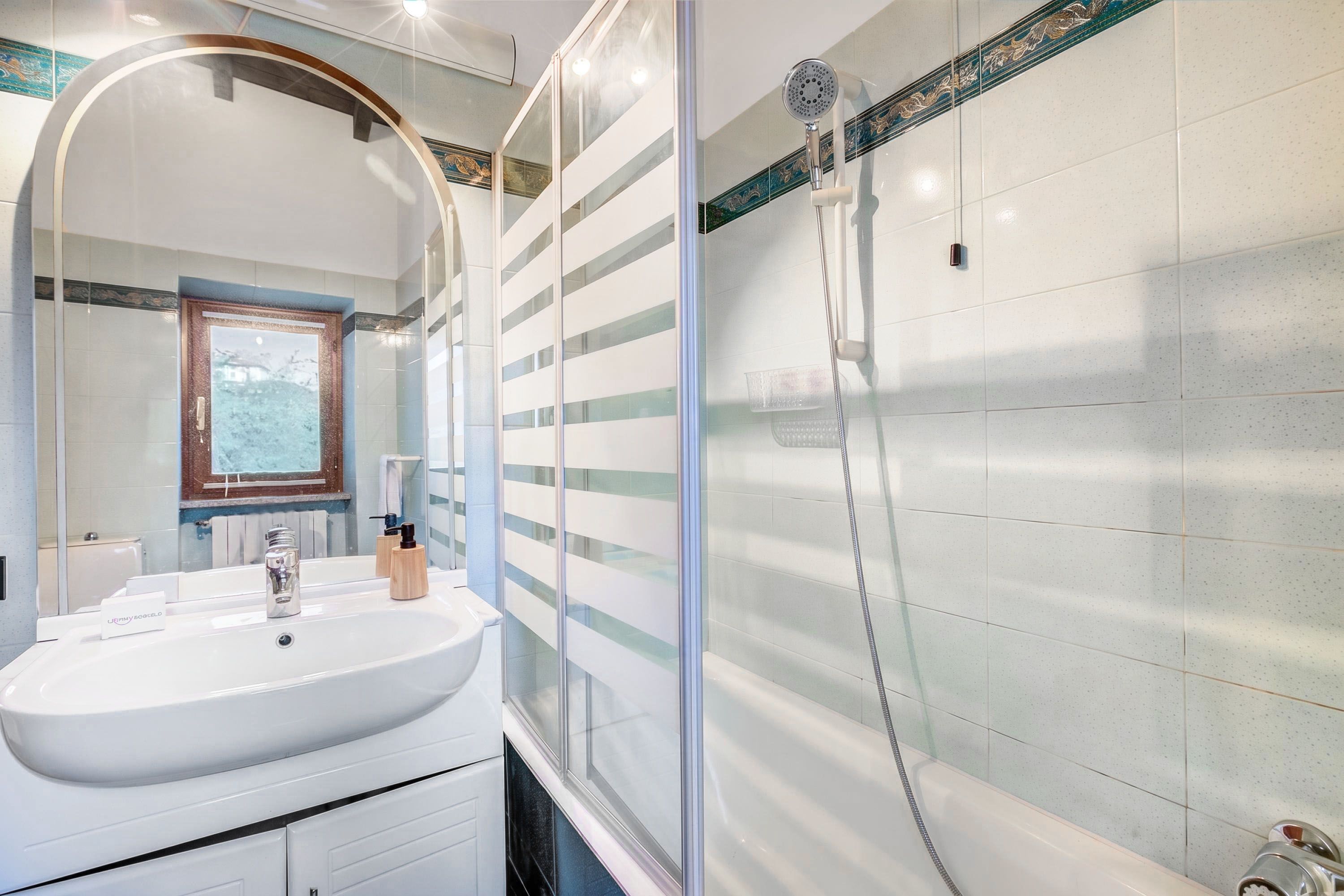 A modern bathroom with a large mirror, a white sink, and a shower area.