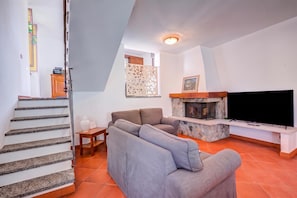 A living room with a sofa, a flat-screen TV, a fireplace, and a staircase. - Casa al Castello in Leggiuno With Garden (Leggiuno)