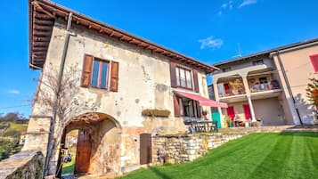 Un bâtiment à deux étages avec une façade en pierre, une porte en bois et un petit balcon surmonté d’un auvent rouge.