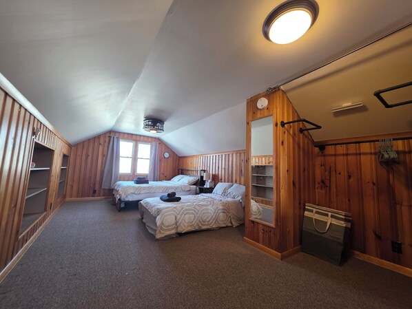 A cozy attic bedroom with two beds, wooden walls, a sloped ceiling, and a large window. - Cozy House in Amherst NY, near UB, Niagara Falls,Airport, Bill Stadium (Buffalo)