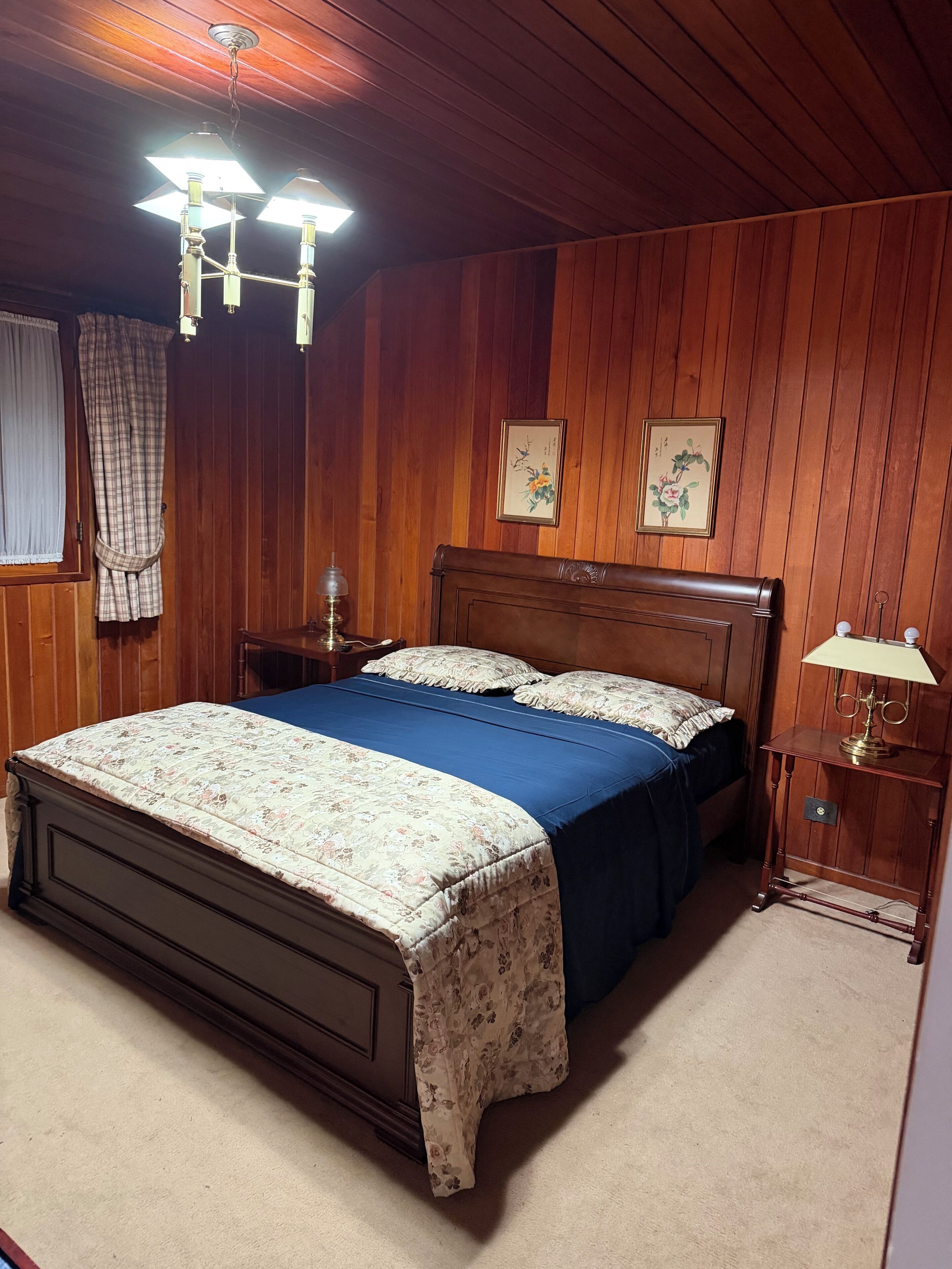 Un dormitorio con paneles de madera, una cama grande, dos lámparas de pared y una mesita de noche con lámpara.
