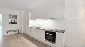 A modern kitchen with white cabinetry, a built-in dishwasher, and a bench in the corner. - City Apartment in Copenhagen with 2 bedrooms sleeps 4 (Copenhagen)