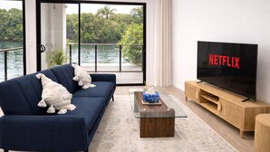 Un salón con un sofá azul oscuro, una mesa de centro de vidrio, un mueble bajo para televisión de madera y un televisor de pantalla plana grande que muestra el logotipo de Netflix.