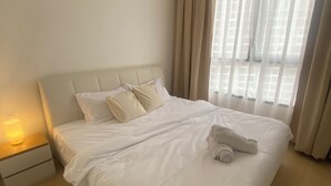 A neatly made bed with white linens, a bedside lamp, and a window with curtains. - becentral residence i-city (Shah Alam)