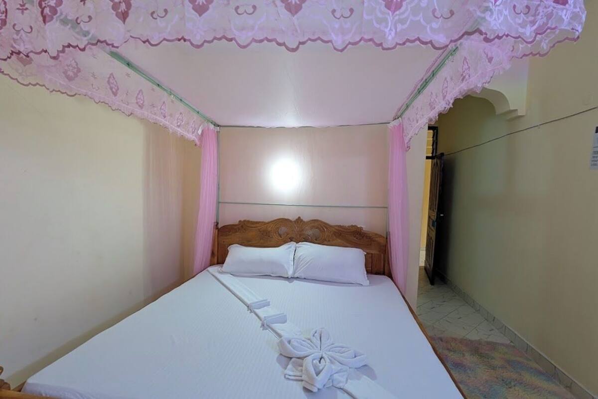 A neatly made bed with white linens and a floral-patterned canopy.