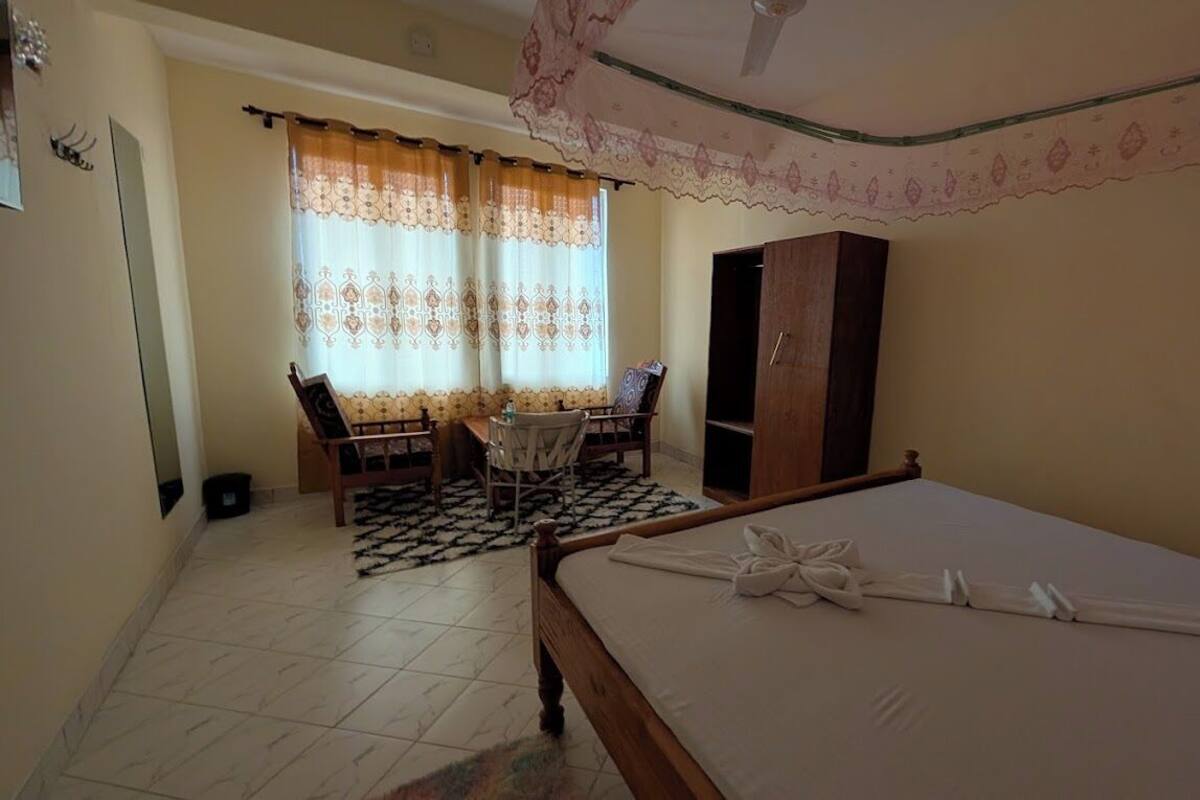 A bedroom with a bed, a wardrobe, a desk with a chair, and a window with curtains.