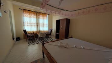 A bedroom with a bed, a wardrobe, a desk with a chair, and a window with curtains.
