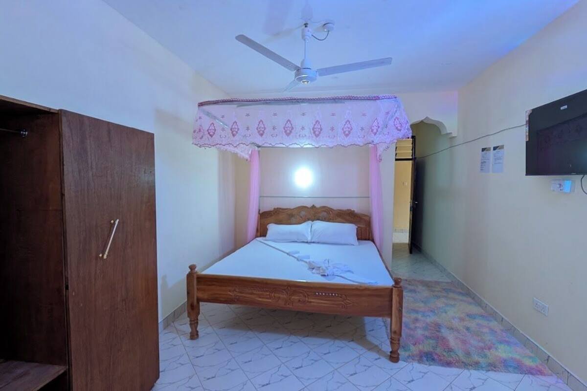 A bedroom with a wooden bed, a ceiling fan, a television mounted on the wall, and a wardrobe.