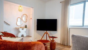 Ein modernes Wohnzimmer mit Flachbildfernseher, einer Couch, einem Sessel und einem kleinen Tisch.