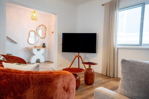 Ein modernes Wohnzimmer mit Flachbildfernseher, einer Couch, einem Sessel und einem kleinen Tisch.