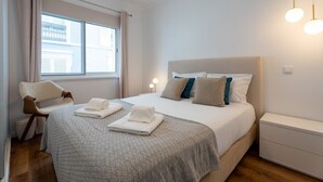 Ein Schlafzimmer mit Bett, Nachttischen, einem Sessel und einem Fenster.