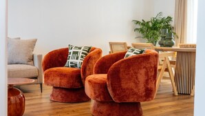 Ein modernes Wohnzimmer mit einer Couch, zwei Samt-Sessel, einem Holztisch und einer Topfpflanze.