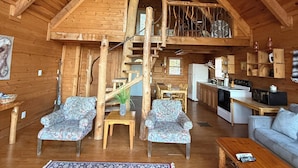 Un'ampia stanza in stile loft con soffitto alto, travi a vista, una scala centrale, zona pranzo e cucina.