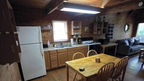 L'interno accogliente di una baita rustica con un tavolo da pranzo in legno, sedie, un frigorifero, un fornello e un divano.