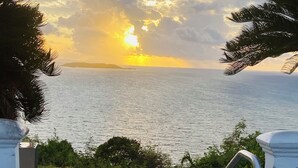 Eine Person im Badeanzug und Hut steht in einer Badewanne mit Blick auf den Ozean und den Sonnenuntergang.