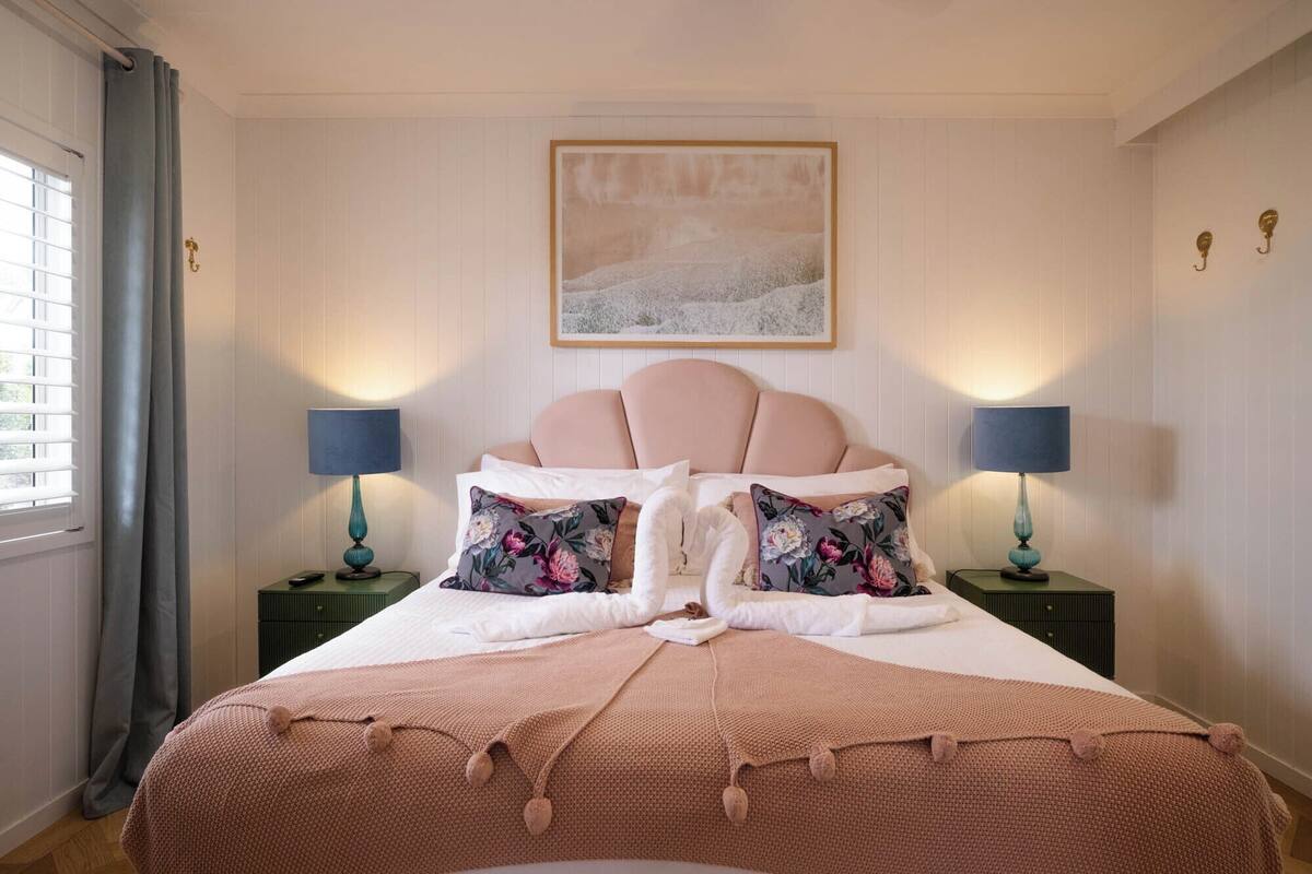 A neatly made bed with a pink headboard, two matching lamps, and floral pillows.