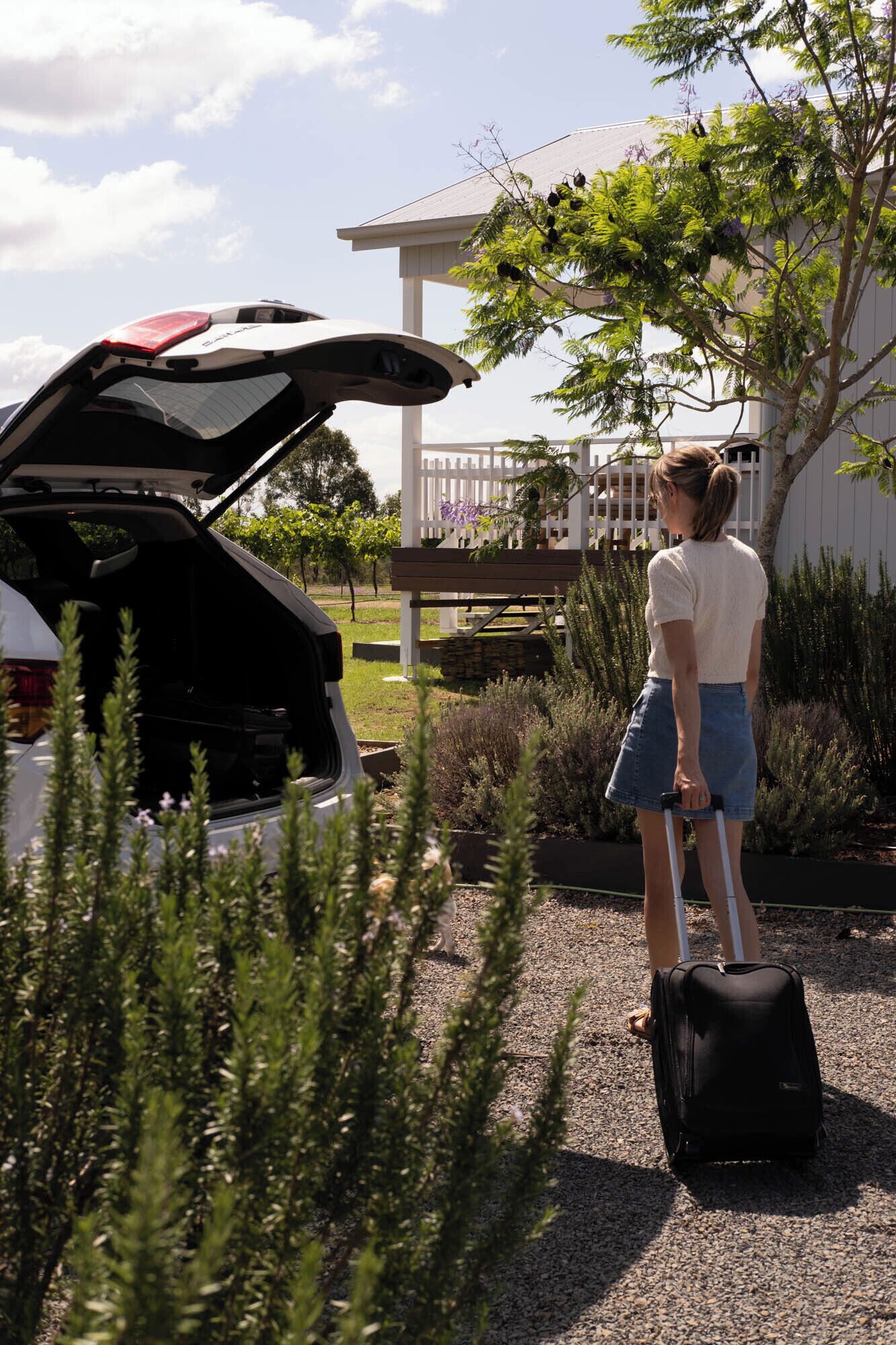 A person standing next to an open car trunk with a suitcase nearby.