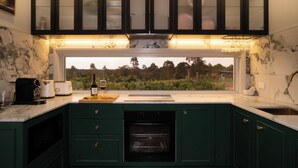 A kitchen with a built-in oven, a window overlooking greenery, and a countertop with a toaster and a wine bottle. - Lusso Retreats (Moffatdale)