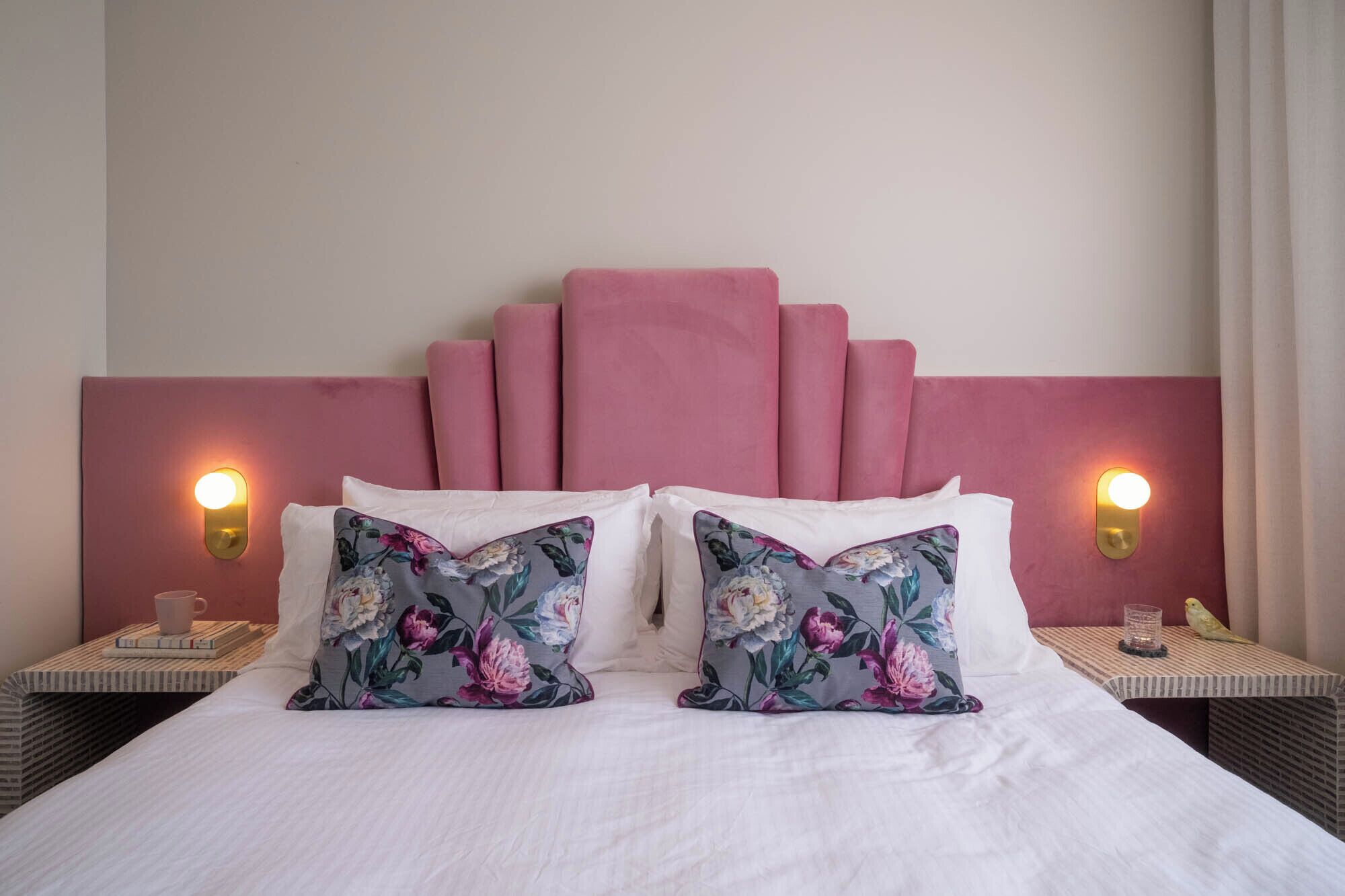 Une chambre d’hôtel avec un lit, deux tables de chevet et une tête de lit agrémentée d’un coussin rose.