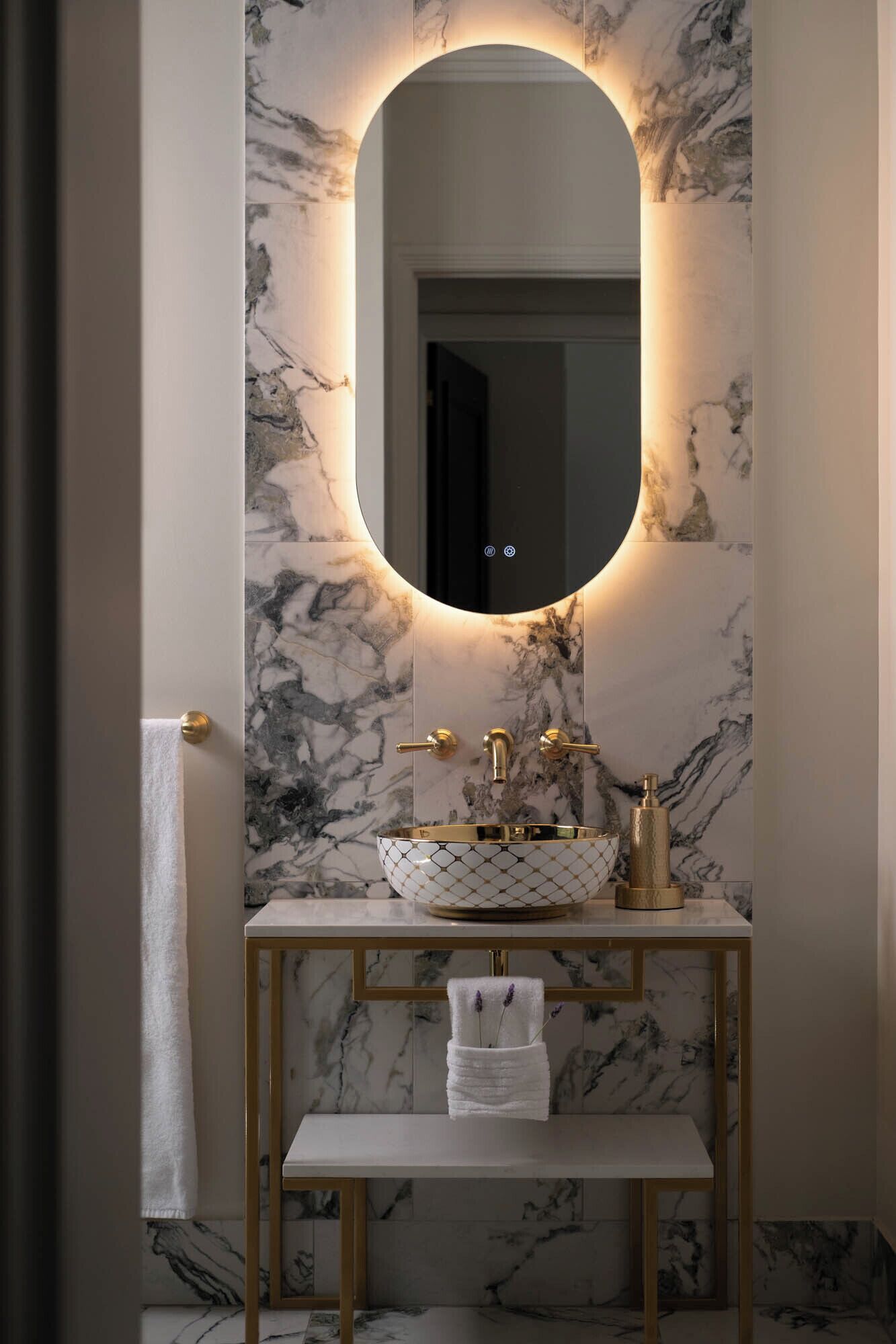 A bathroom with a marble wall, a gold-framed vanity, a round mirror, and a white sink.