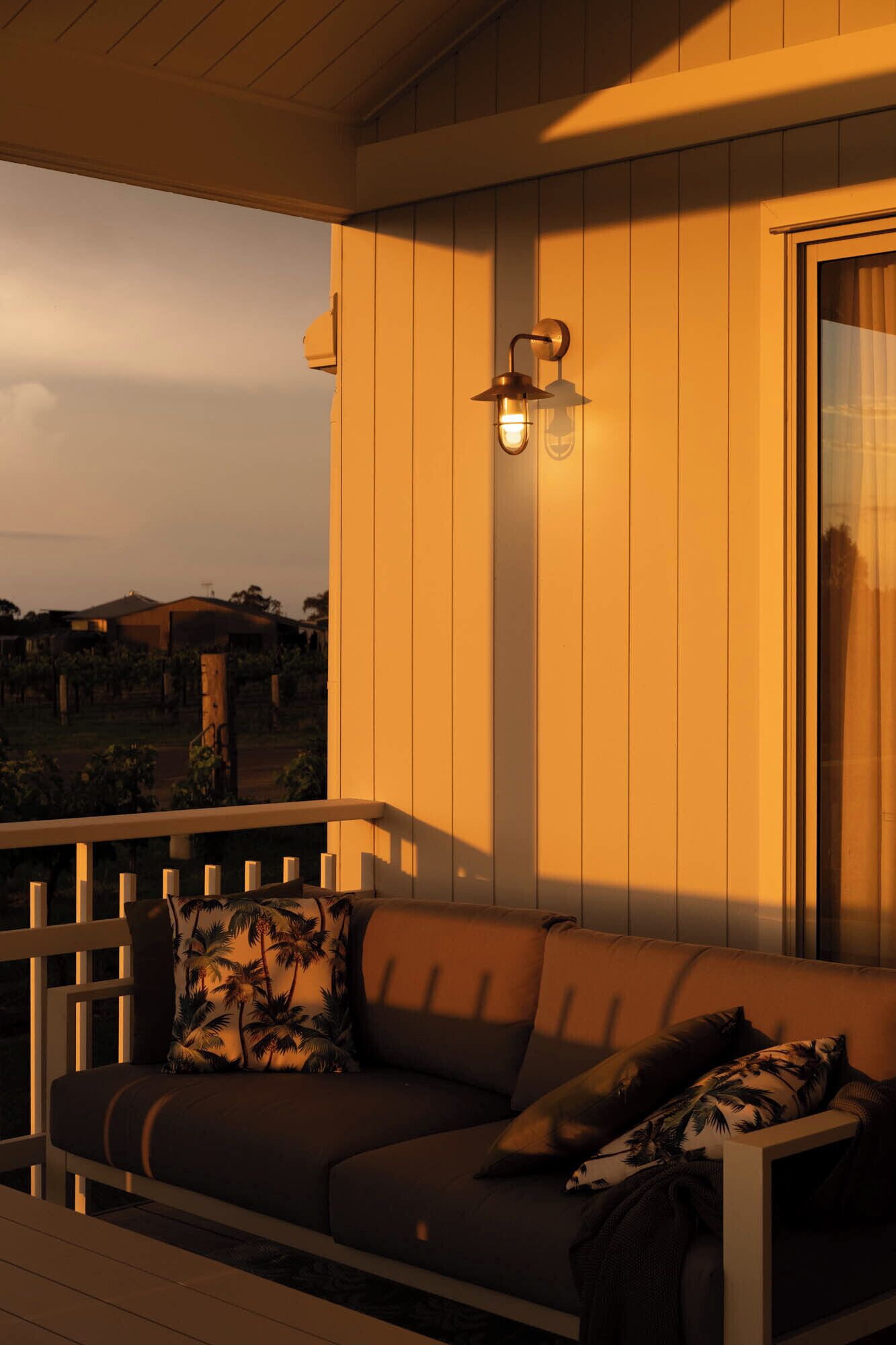 Une véranda en bois avec un coin salon agrémenté de coussins, un luminaire fixé au mur et une vue sur le paysage environnant.