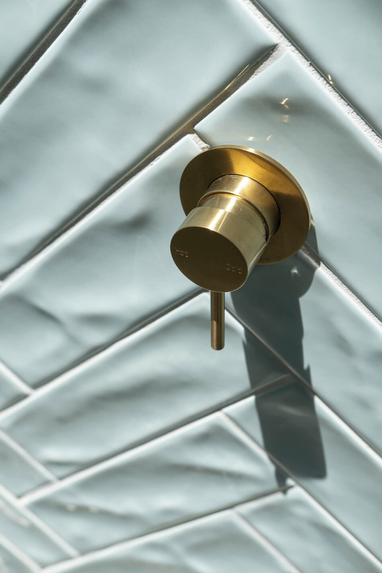 A brass door handle against a tiled wall.