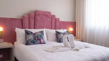 Una cama bien hecha con almohadas estampadas con motivos florales, un cabecero rosa y un ventilador de techo.