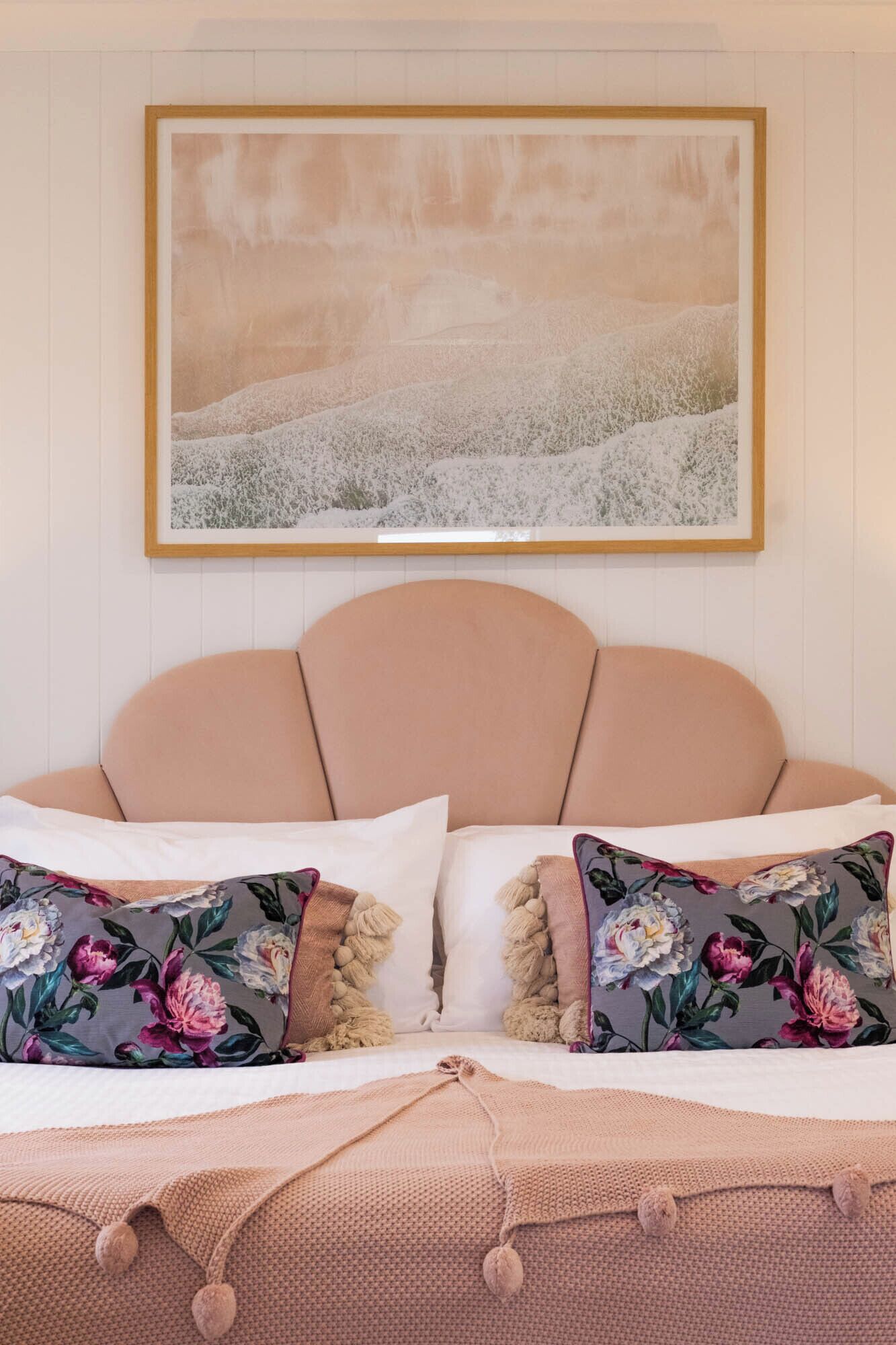 A bedroom with a bed, two pillows, a blanket, and a painting on the wall.