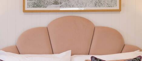 A bedroom with a bed, two pillows, a blanket, and a painting on the wall.