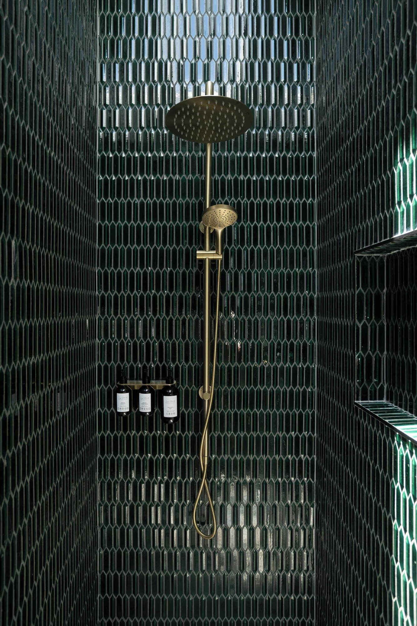 A shower with a rain showerhead and handheld showerhead, surrounded by a hexagonal patterned wall.