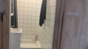 A small bathroom with white tiles, a white sink, a towel rack, and a shower area. - Clean and well-kept room 5min from centraal station (Amsterdam)