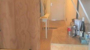 A wooden interior with a white door, a small table with a vase, and a counter with kitchen items. - Clean and well-kept room 5min from centraal station (Amsterdam)