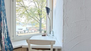 A small room with a white desk and chair, a lamp, and a window overlooking a tree and buildings. - Clean and well-kept room 5min from centraal station (Amsterdam)