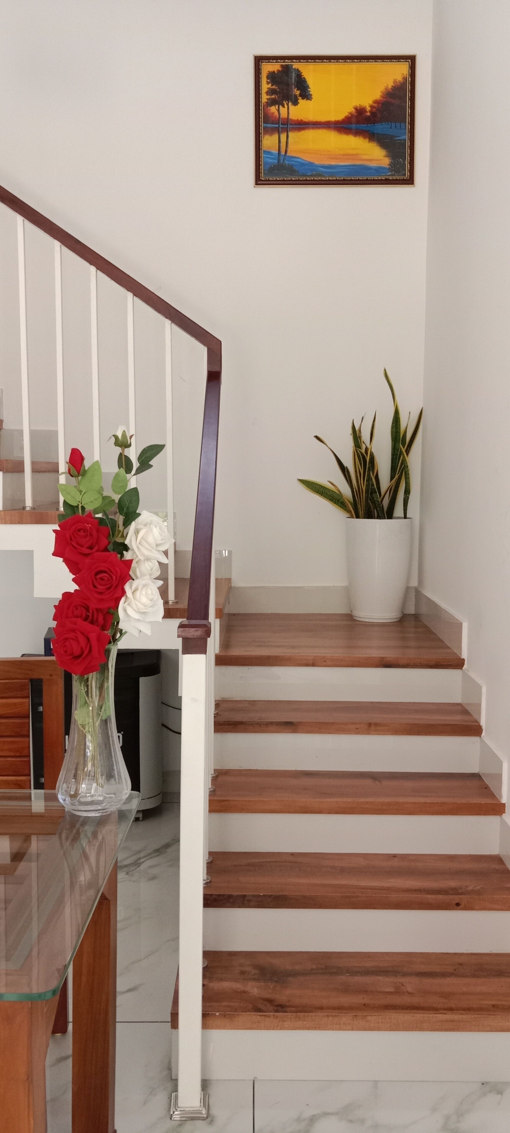 A staircase with wooden steps and white railings, a vase with red and white roses, and a potted plant on the landing.