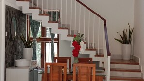Un interior moderno con una escalera, una zona de comedor con sillas de madera y una mesa, y un ventilador de techo.