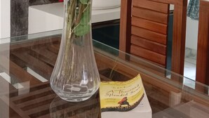 Una mesa de comedor con un jarrón de rosas rojas y blancas, un libro, y un interior moderno con una pared de piedra y una escalera de madera.