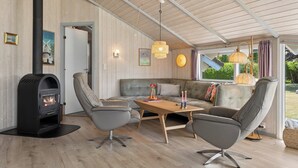 Una sala de estar acogedora con chimenea, sofás de cuero, una mesa de centro de madera y un amplio ventanal con vistas a la vegetación.