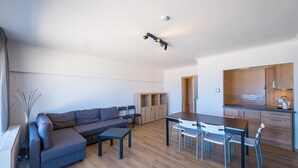 Un salon moderne avec un canapé gris, une table à manger avec des chaises et un coin cuisine doté de meubles en bois et d’un plan de travail.