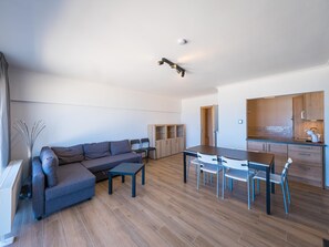 A modern living room with a gray sofa, a dining table with chairs, and a kitchen area with wooden cabinets and a countertop. - Apartment with 3 bedrooms and sea view (Middelkerke)